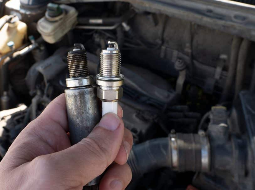 Spark plug replacement - mechanic holding a new spark plug next to an old one